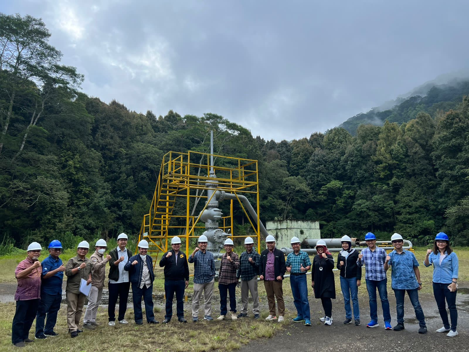 Group photograph in front of wellhead equipment and forest at the project site; brightness and clarity adjusted